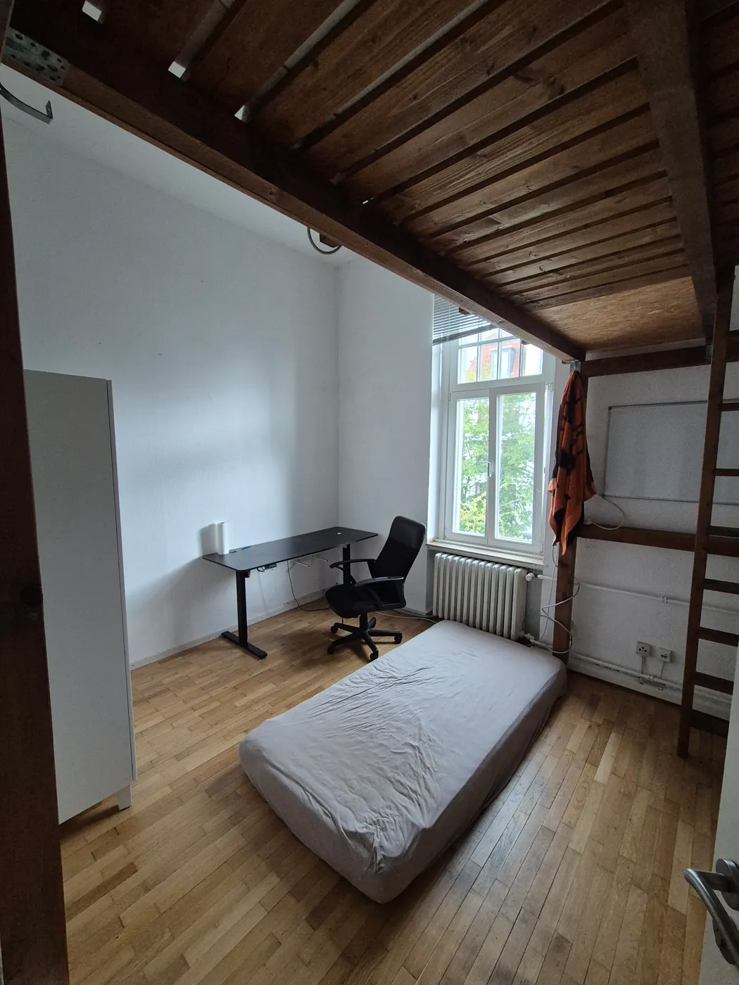 Zimmer mit offener Holzbalkendecke und Schreibtisch am Fenster